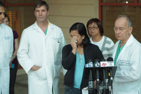 The twins' mother, Ginady Sabuco, wipes away tears of gratitude as she speaks at a news conference Nov. 1 to announce the successful separation of the girls. Surgeons Rohit Khosla, MD, Peter Lorenz, MD, and Gary Hartman, MD, (L-R, in white coats) joined her.