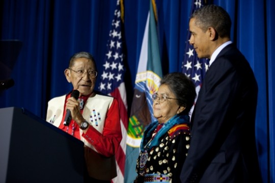 President Barack Obama is joined onstage by his adopted Native American parents, Hartford "Sonny" Black Eagle and Mary Black Eagle, during the 2011 Tribal Nations Conference at the Department of Interior, Washington, D.C., Dec. 2, 2011. (Official White House Photo by Pete Souza)