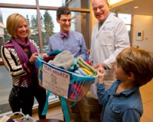 Andrea Fisher's friend Sharon Thomas, left, and her son Miles, right, present the basket of caps to Alexander Colevas, MD (center left), and Douglas Blayney, MD, Medical Director, Stanford Cancer Center (center right).