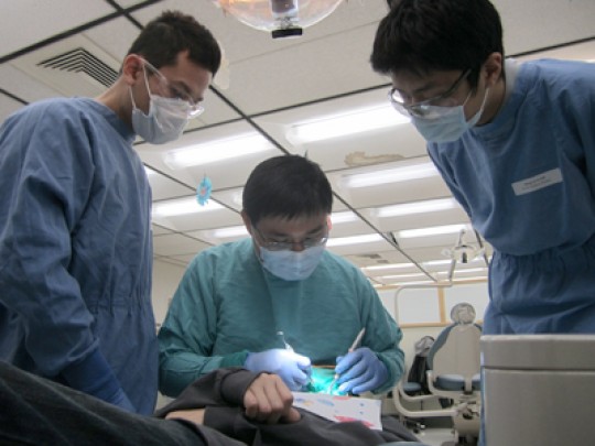 Brent Lin, DMD, cleans a patient’s teeth at the UCSF School of Dentistry Dental Clinic as two dental students observe.